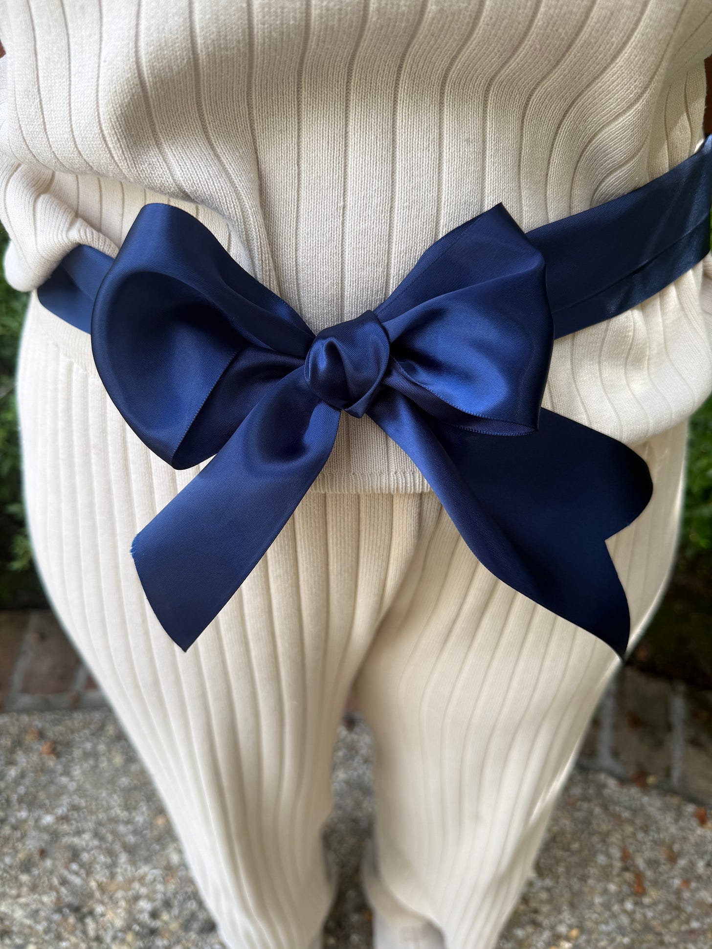 Completed navy satin bow tied at the waist of white ribbed pants
