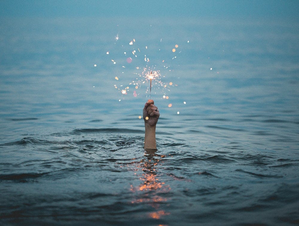 person submerged on body of water holding sparkler person submerged on body of water holding sparkler