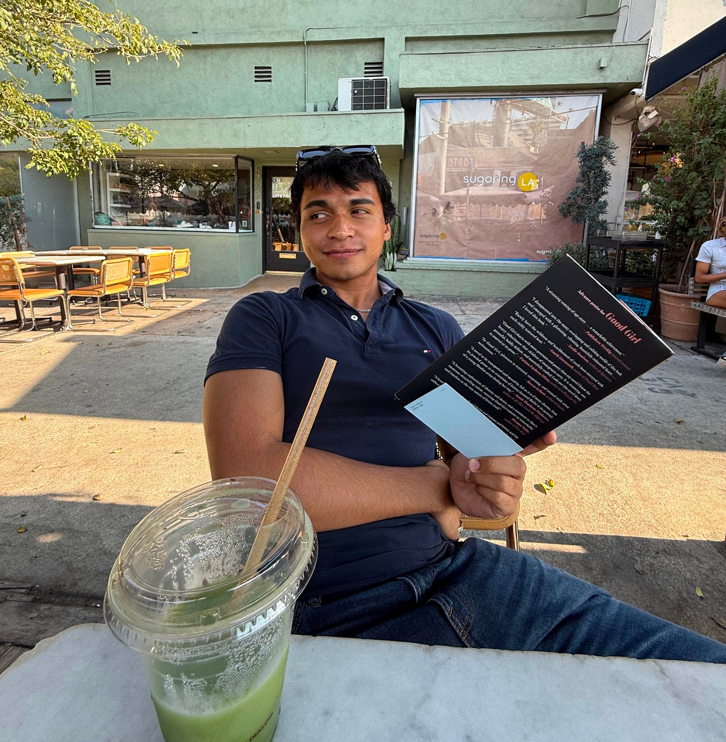 Jalen sits outside holding a book with a matcha latte