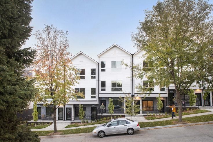This may contain: a car is parked in front of some white buildings with trees on the side walk