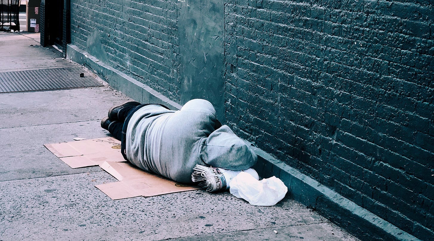 Person sleeping on sidewalk next to building. Person sleeping on sidewalk next to building.