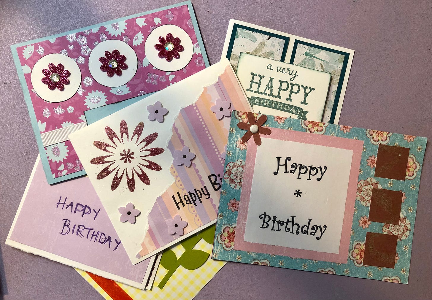 Some beautiful handmade birthday cards spread out on a light purple surface.