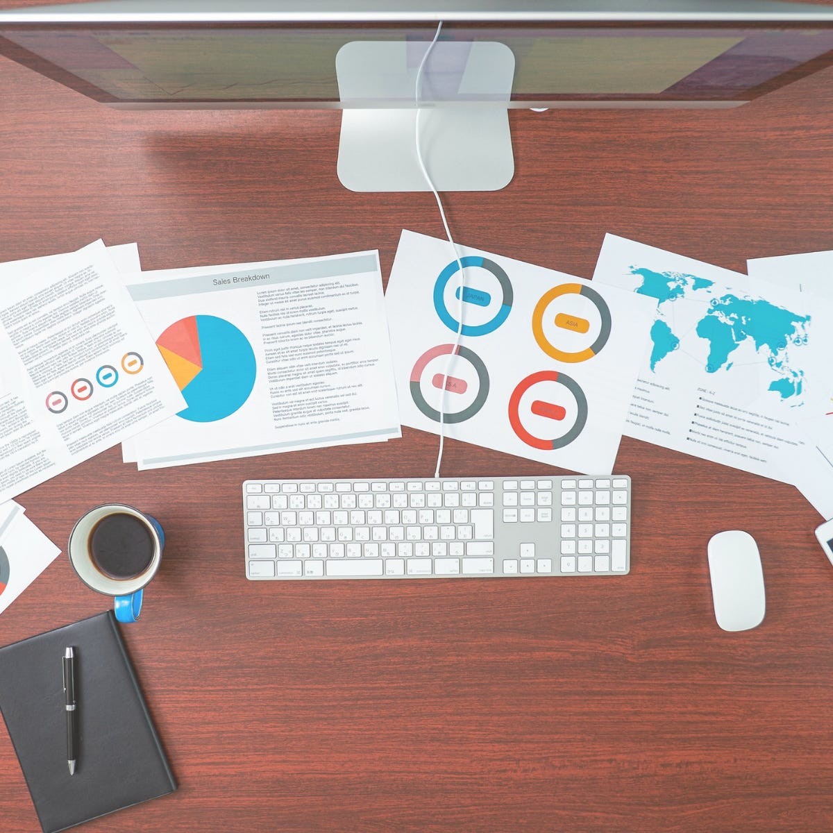 Top view of a desk with a computer, coffee mug, and printed charts showing graphs and global data, representing analysis of LinkedIn impressions and engagement results.