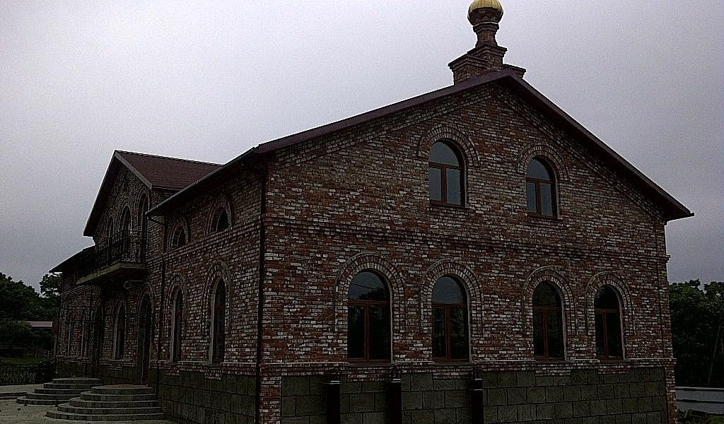 Two-story red-and-tan brick building with rows of arched windows and a small gold dome, under an overcast sky.