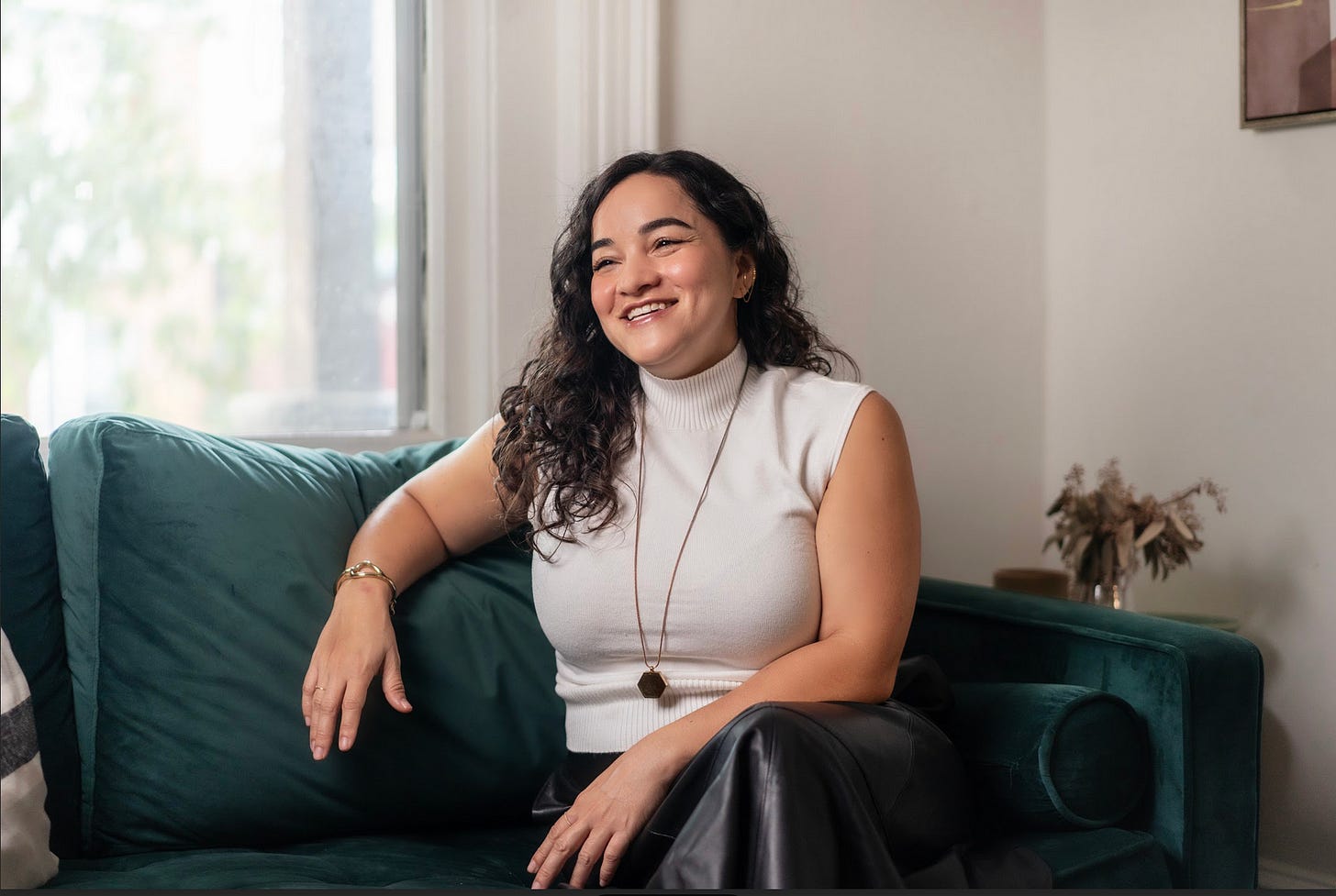 Corinne Low sitting on couch. She is an Asian woman smiling and relaxed, longish curly hair, wearing sleeveless blouse and a necklace. there's a window with sunlight streaming in Corinne Low sitting on couch. She is an Asian woman smiling and relaxed, longish curly hair, wearing sleeveless blouse and a necklace. there's a window with sunlight streaming in