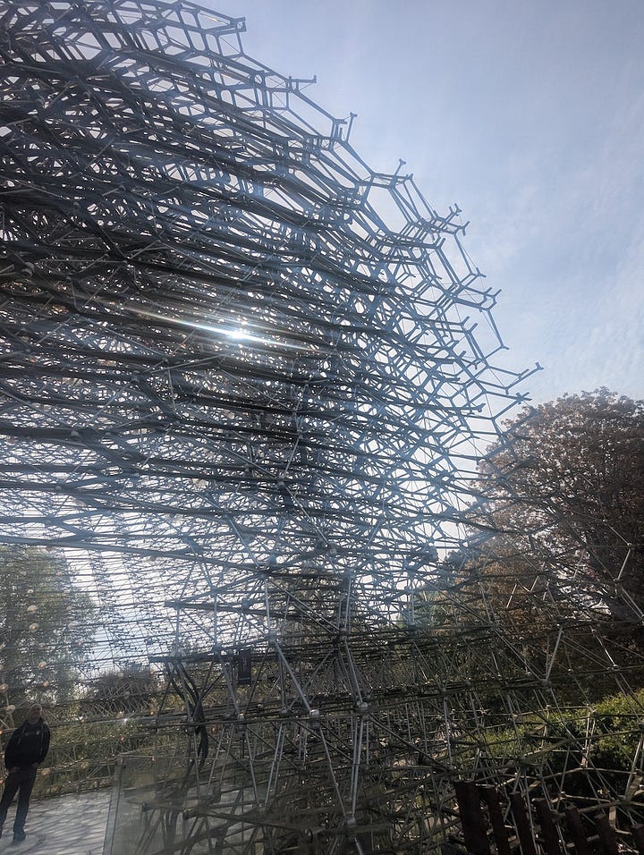 Three views of The Hive at Kew Gardens, a large aluminium lattice structure rising from a grassy landscape, shown from a distance, from beneath, and looking up through its circular interior.