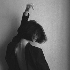 This may contain: a black and white photo of a woman leaning against a wall with her arms in the air