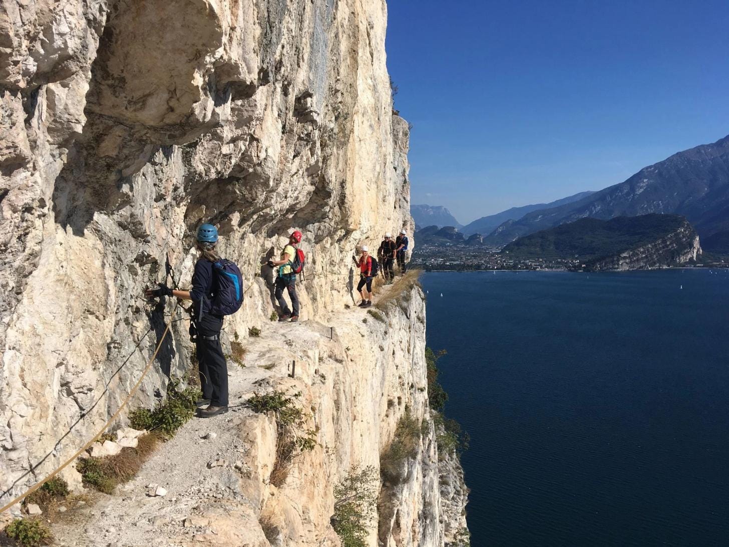 A group of people climbing a via ferrata route near Arco, Italy, using fixed cables and ladders above Lake Garda. A group of people climbing a via ferrata route near Arco, Italy, using fixed cables and ladders above Lake Garda.
