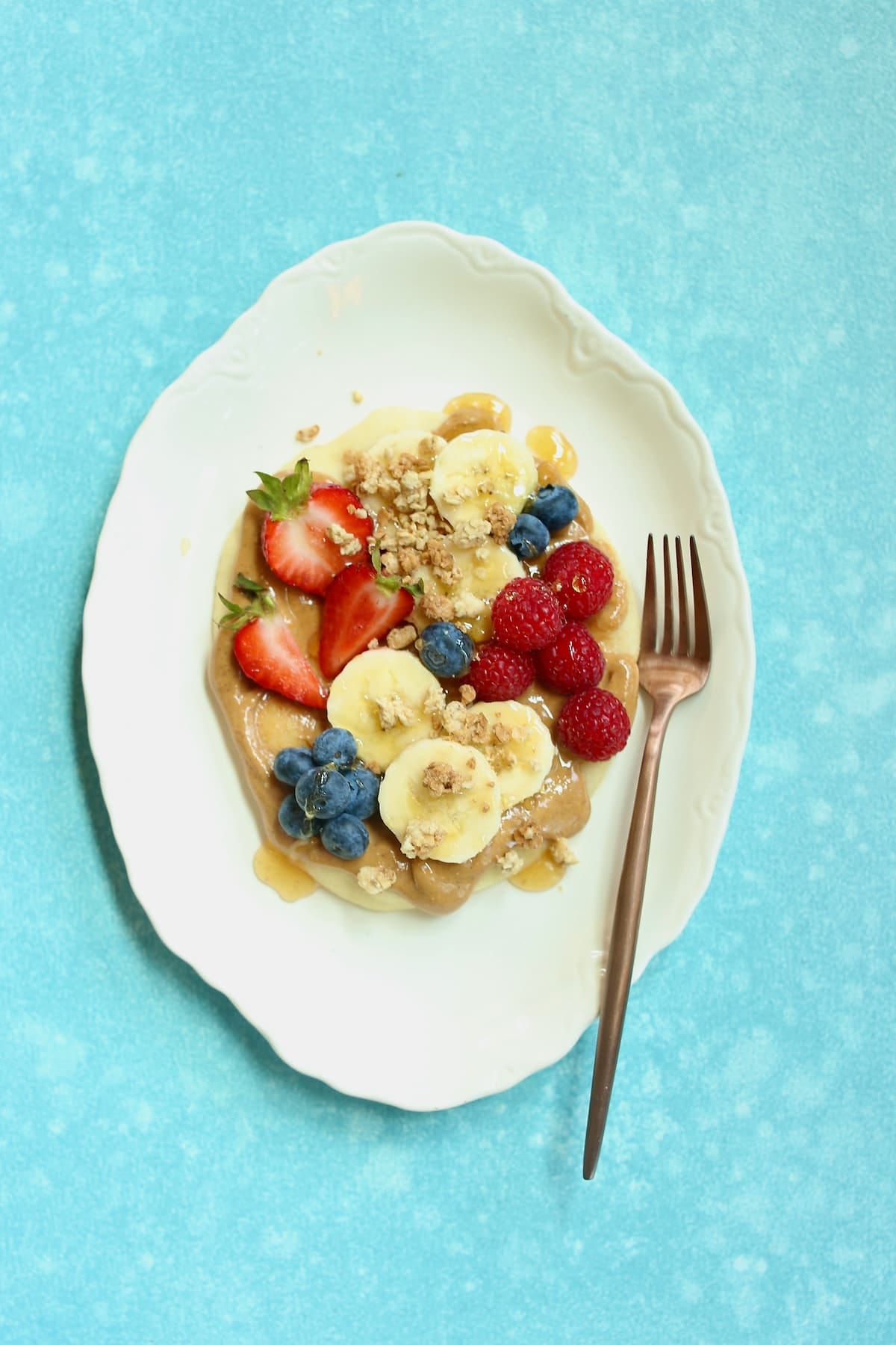 a white plate of naan with berries and nut butter on top.