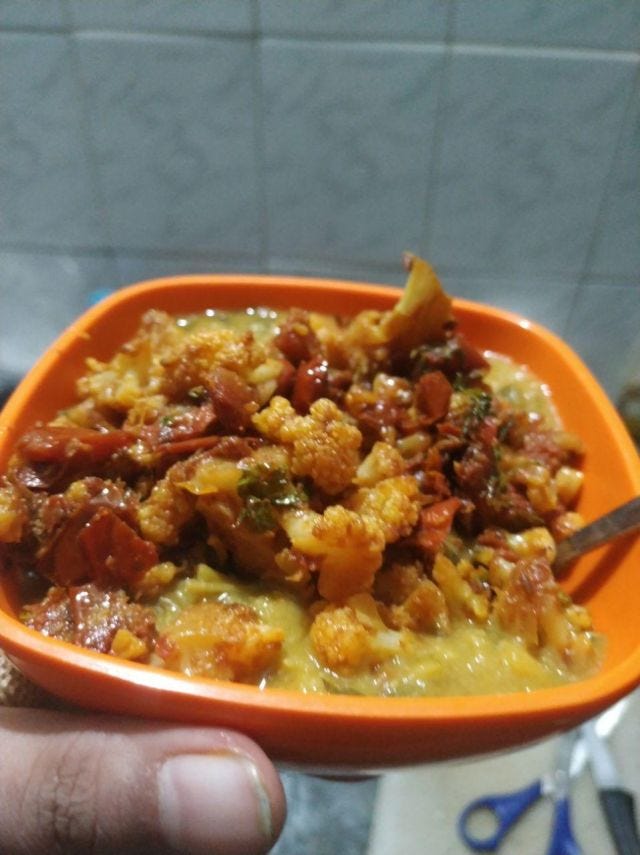 An orange bowl with cauliflower cooked alongside tomatoes.