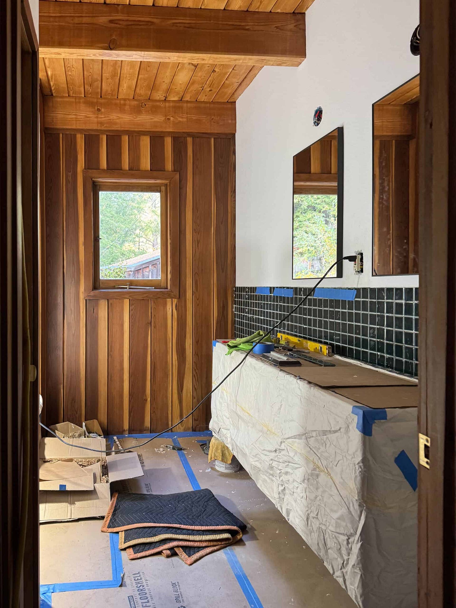 Construction work is in progress on the bathroom, with the vanity covered up and tile going up the wall halfway. 