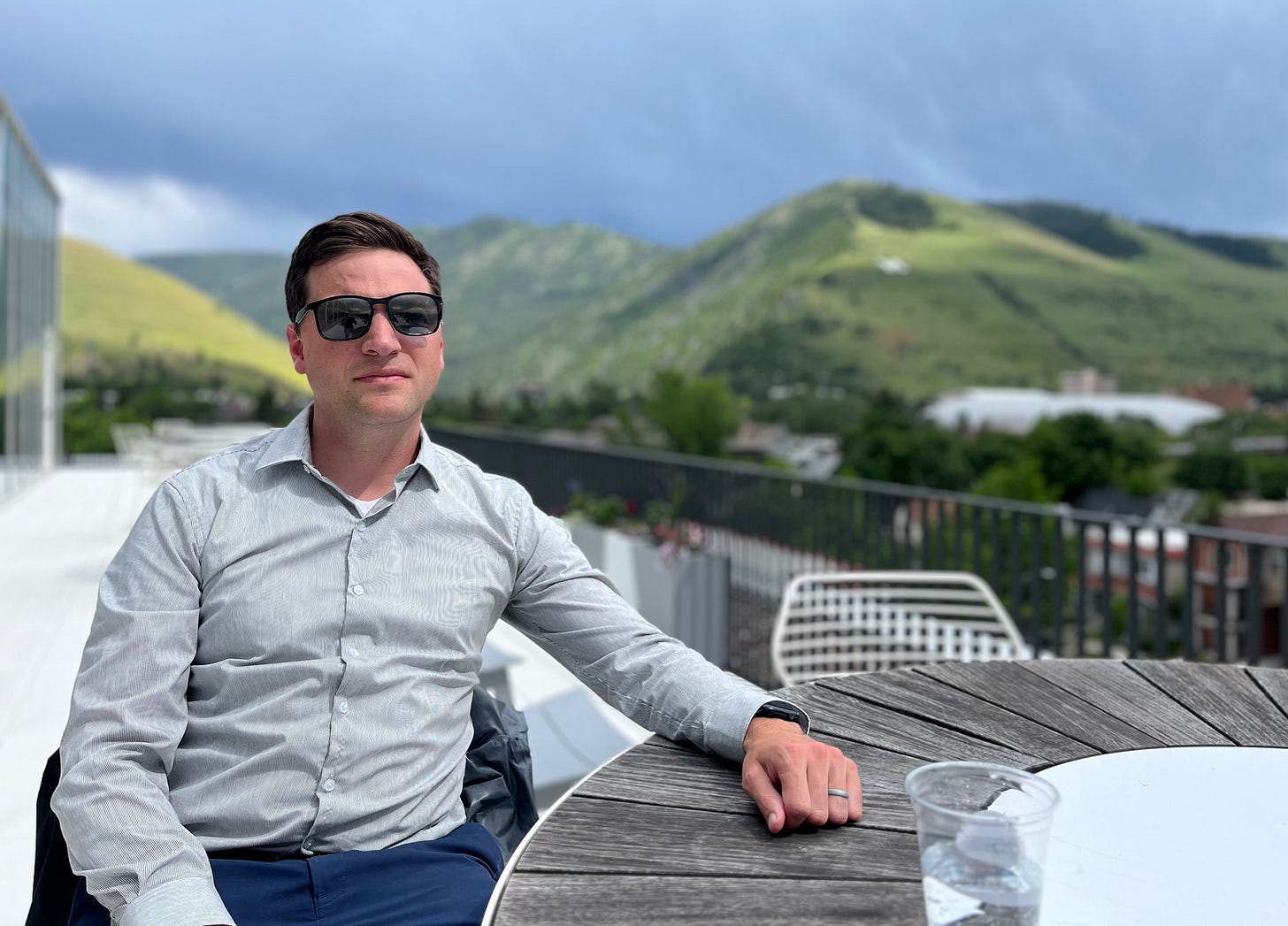 man in sunglasses on rooftop patio with mountains behind him man in sunglasses on rooftop patio with mountains behind him