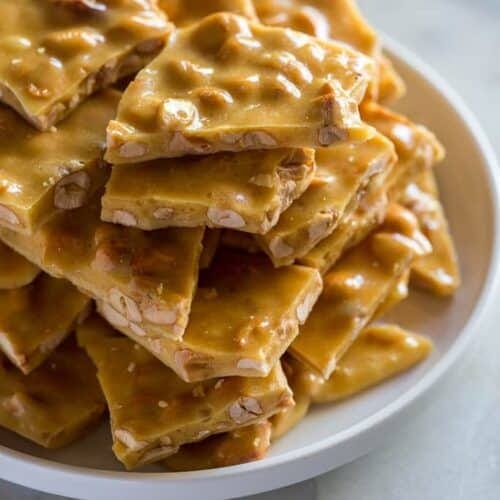 A plate with pieces of peanut brittle stacked on it. A plate with pieces of peanut brittle stacked on it.