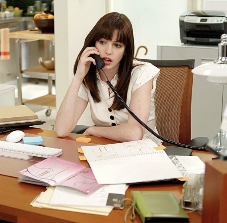 This may contain: a woman sitting at a desk talking on the phone