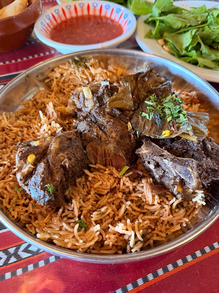 four photos, including: a plate of prawns with mini paratha, Anela standing in front of a mosque with tan stone walls around her, an ornate huge lamp with filigree and light shining through, and a plate of Shuwa, a common dish in Oman of marinated meat that has been cooked underground and served with rice.