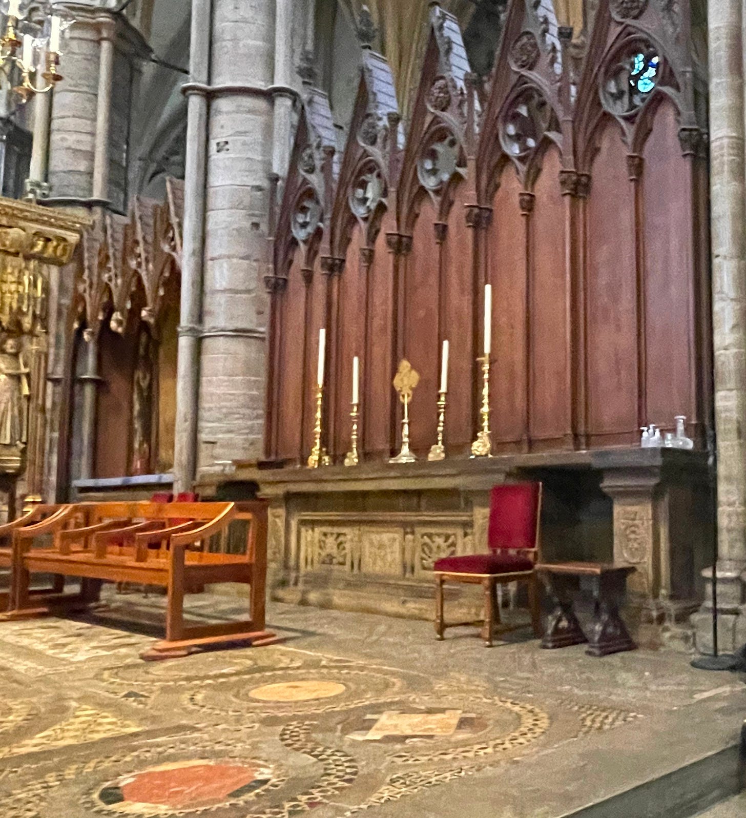 A cathedral interior showing a dark brown wooden screen, a stone tomb underneath, and a mosaic floor