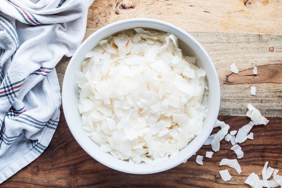 Bowl of large coconut flakes sitting on a wooden surface with a white kitchen towel. Bowl of large coconut flakes sitting on a wooden surface with a white kitchen towel.