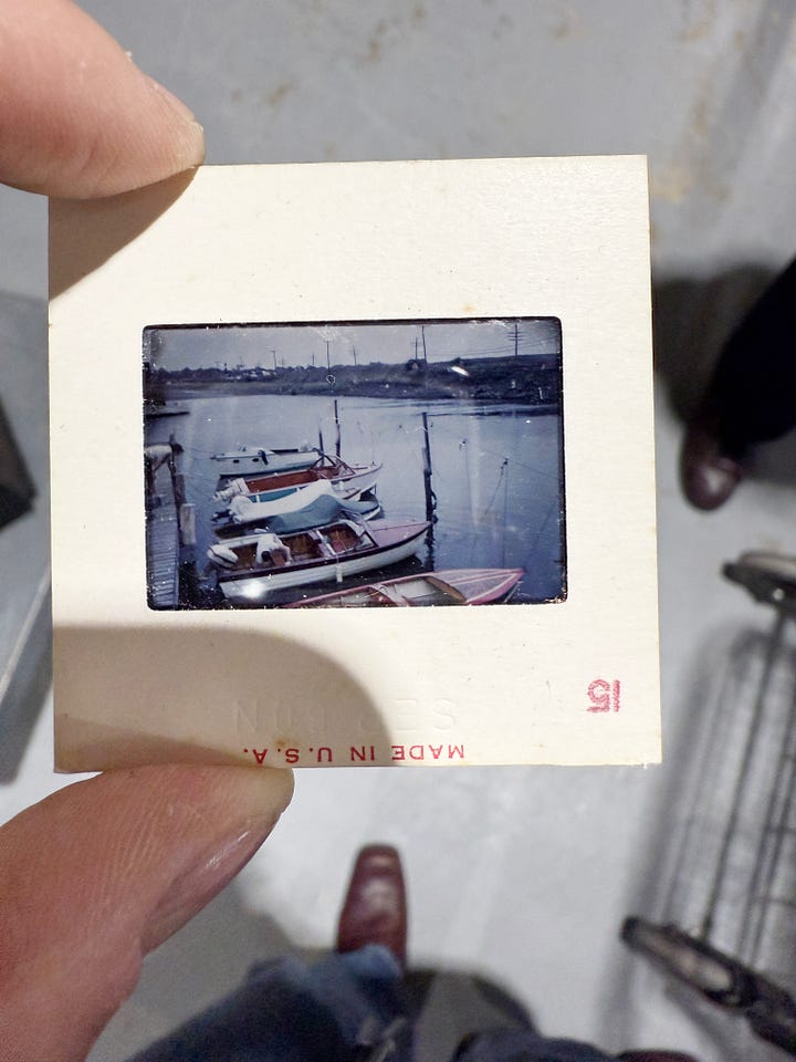 Collection of vintage Kodak slides showing various Caribbean vacation scenes including boats, people on docks, and sailing, plus a black vintage slide viewer device in a shopping cart