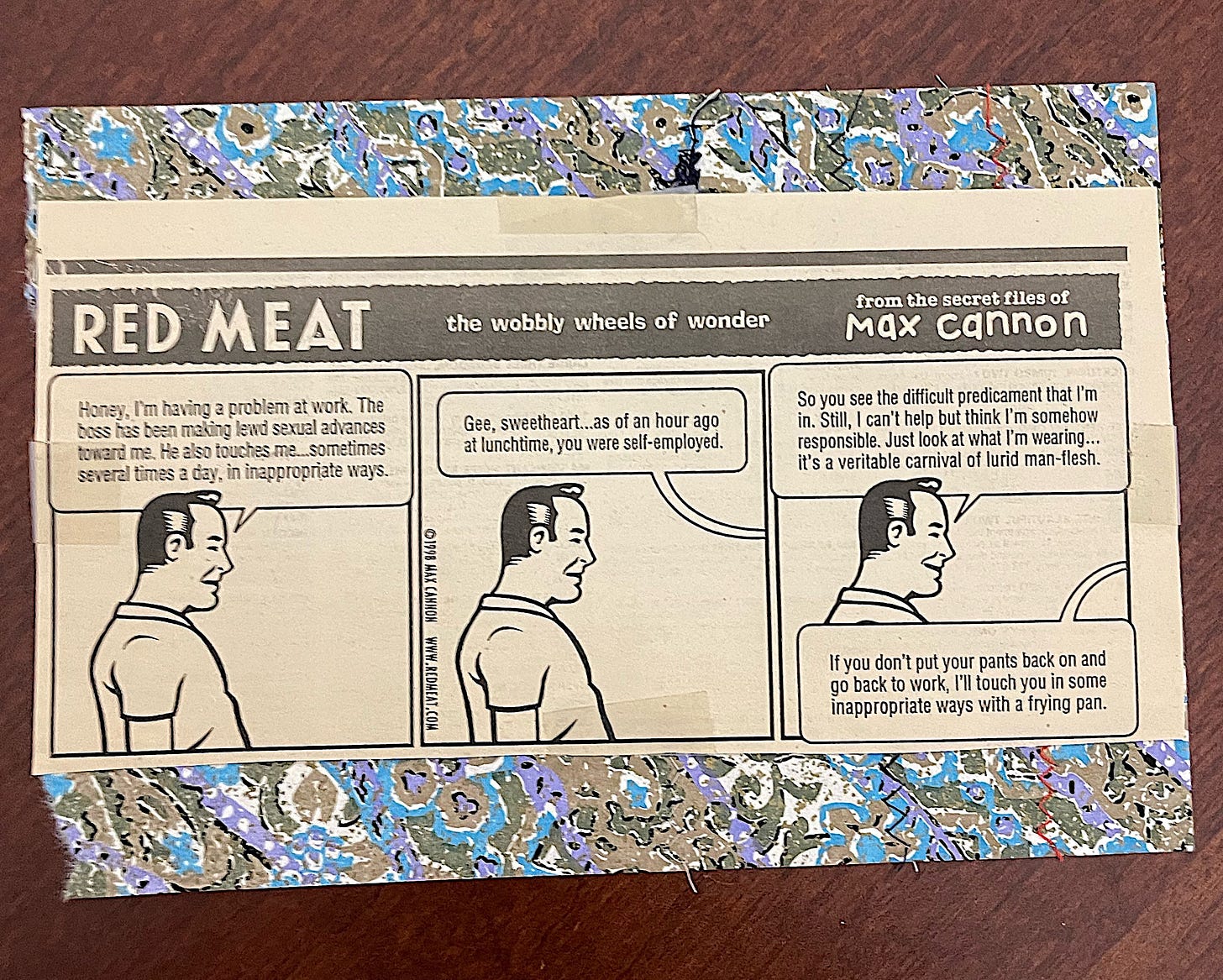 A cut-out comic strip from the Red Meat series by Max Cannon, titled "The Wobbly Wheels of Wonder," taped onto a background of blue, silver, and purple patterned paper. The strip features three black-and-white panels with a man speaking humorously about workplace sexual harassment in an absurd, deadpan tone. The comic rests on a reddish wooden surface. A cut-out comic strip from the Red Meat series by Max Cannon, titled "The Wobbly Wheels of Wonder," taped onto a background of blue, silver, and purple patterned paper. The strip features three black-and-white panels with a man speaking humorously about workplace sexual harassment in an absurd, deadpan tone. The comic rests on a reddish wooden surface.