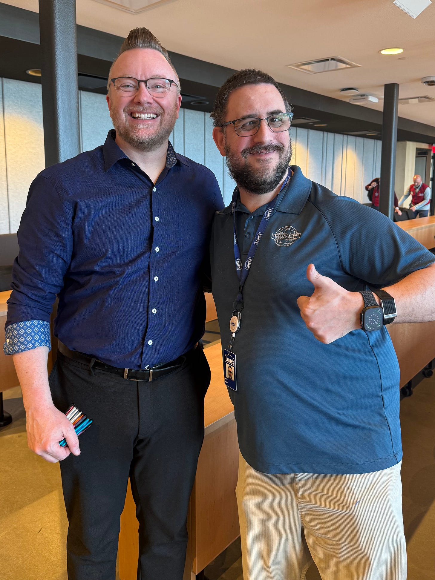 James Geiger stands smiling beside keynote speaker Phil Hansen after a quarterly Lowe’s Townhall. Both are indoors in a meeting space, smiling at the camera, with James wearing a Lowe’s lanyard and Toastmasters polo while giving a thumbs-up. James Geiger stands smiling beside keynote speaker Phil Hansen after a quarterly Lowe’s Townhall. Both are indoors in a meeting space, smiling at the camera, with James wearing a Lowe’s lanyard and Toastmasters polo while giving a thumbs-up.
