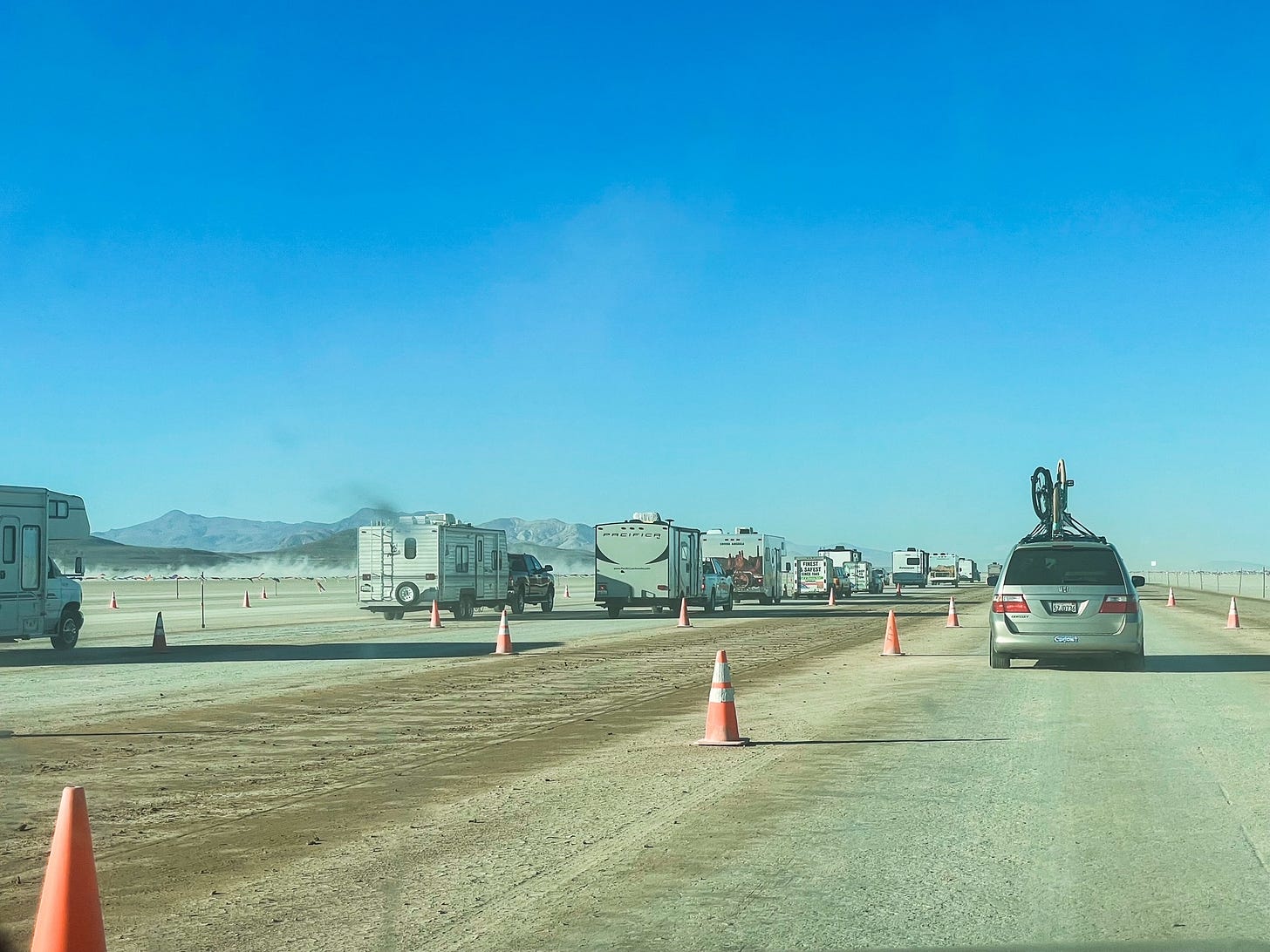 Line of cars and RVs in the desert; mountains behind them