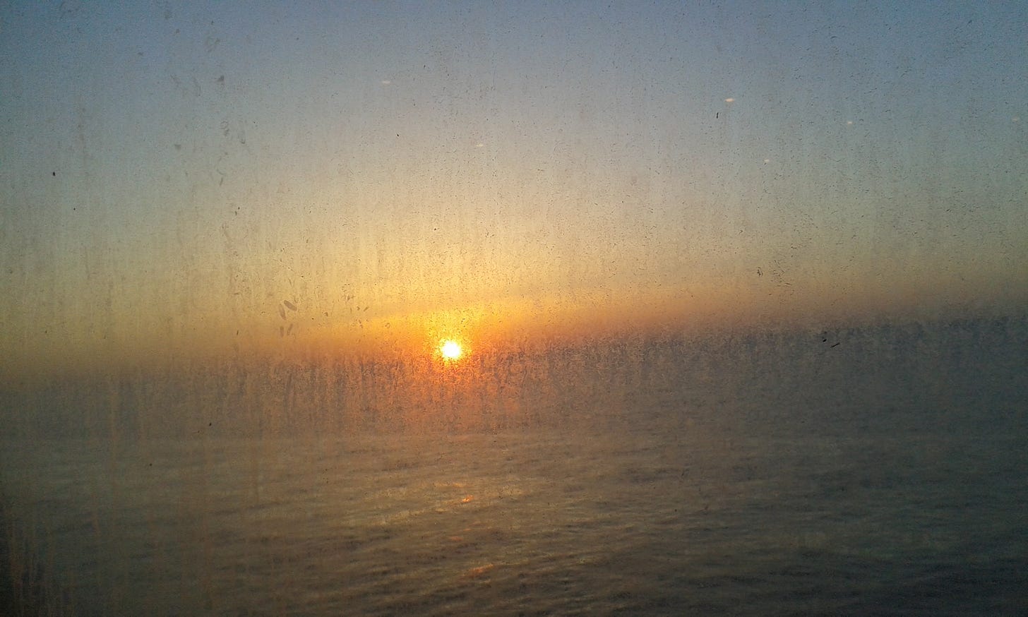 Il sole che sorge sul mare, vista filtrata dall'oblò incrostato del traghetto.