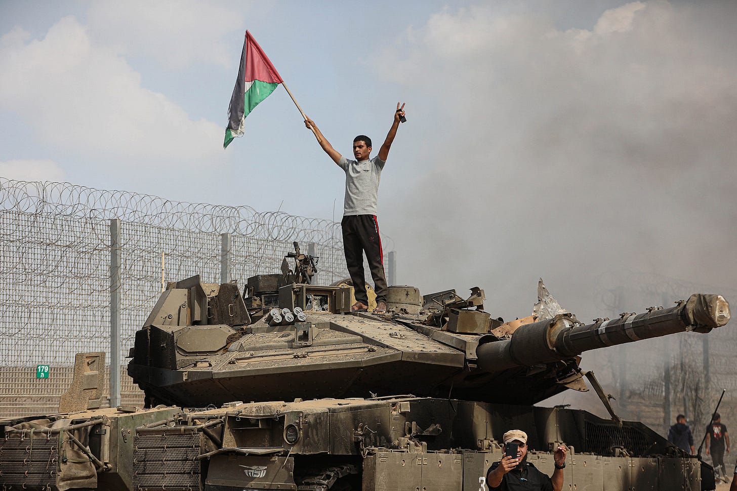 I palestinesi stanno sopra e accanto a un carro armato israeliano all’interno della recinzione di confine con Israele nella città di Khan Younis, nel sud della Striscia di Gaza, il 7 ottobre 2023. (Yousef Mohammed/Flash90) I palestinesi stanno sopra e accanto a un carro armato israeliano all’interno della recinzione di confine con Israele nella città di Khan Younis, nel sud della Striscia di Gaza, il 7 ottobre 2023. (Yousef Mohammed/Flash90)