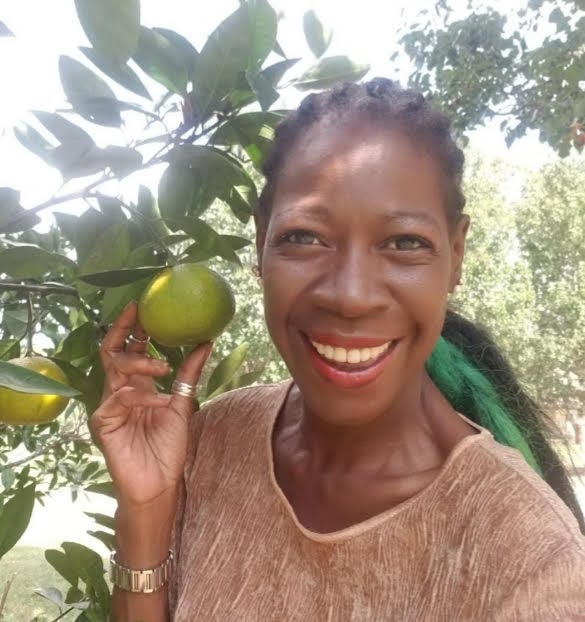Gwen Lynn, a middle-aged woman, holds a plant on a branch and smiles at the camera