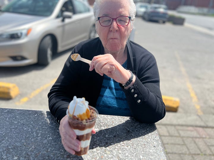 Four adults enjoying an ice cream at a picnic table on a sunny day.