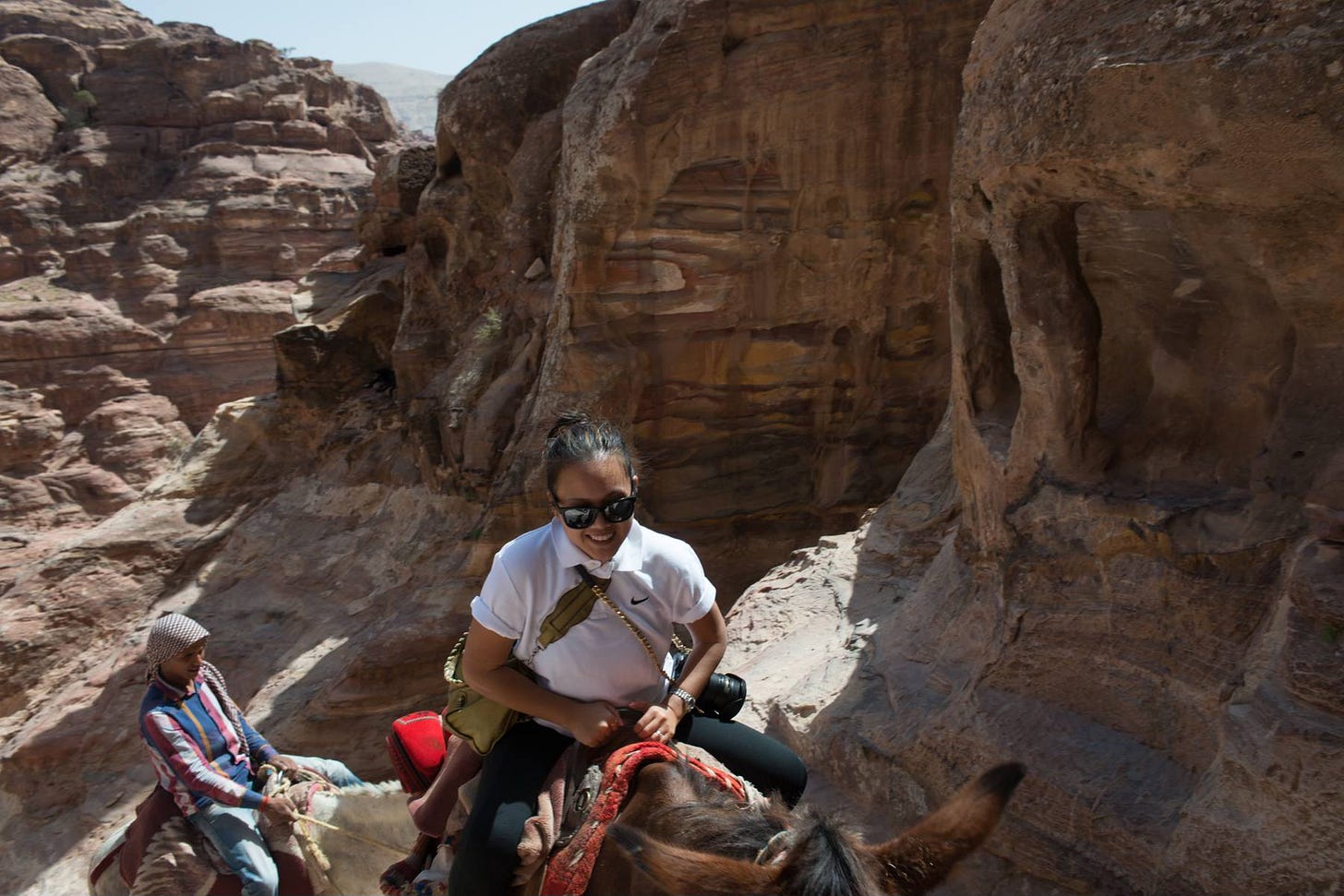 Woman riding a donkey through the ancient rock formations of Petra, Jordan, with a Bedouin guide walking alongside