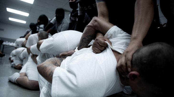 Prisoners in white shirts and shaved heads in a line forceably held down. Their heads are pressing into the backs of the men in front of them Prisoners in white shirts and shaved heads in a line forceably held down. Their heads are pressing into the backs of the men in front of them