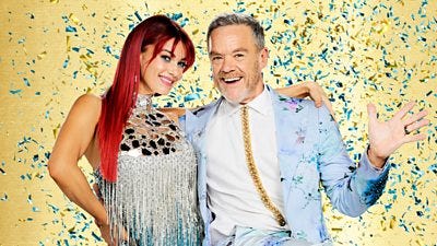 Diane wears a shimmering silver and blue fringe trimmed dress while Stefan wears a white shirt with a stripe of gold beneath a blue floral patterned suit