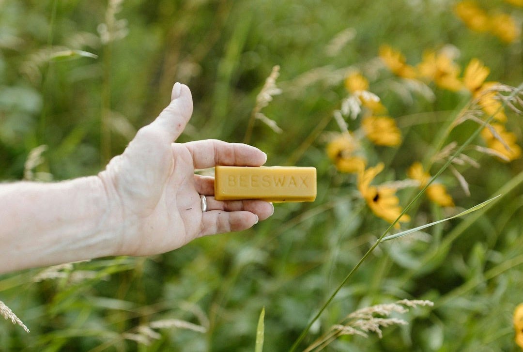 A hand holding a piece of yellow paper in a field of yellow flowers