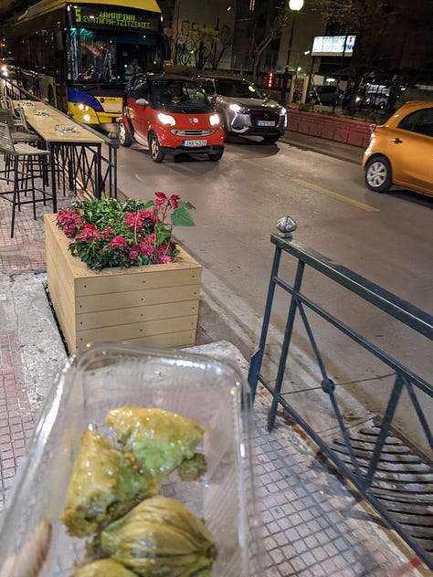 Baklava in a to-go container, a sign describing Greek ruins, and a sign in a pizza shop saying "I will always eat pizza. Always"