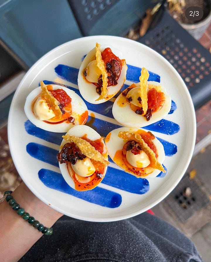 "Close-up van een gevuld ei gegarneerd met crispy chili-olie, pittige kimchi-saus en een krokante wonton topping, geserveerd op een gestreept bord.