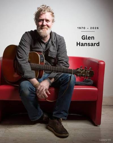 Photo of Glen Hansard sitting on a couch with his guitar and the dates 1970-2026 laid over the image