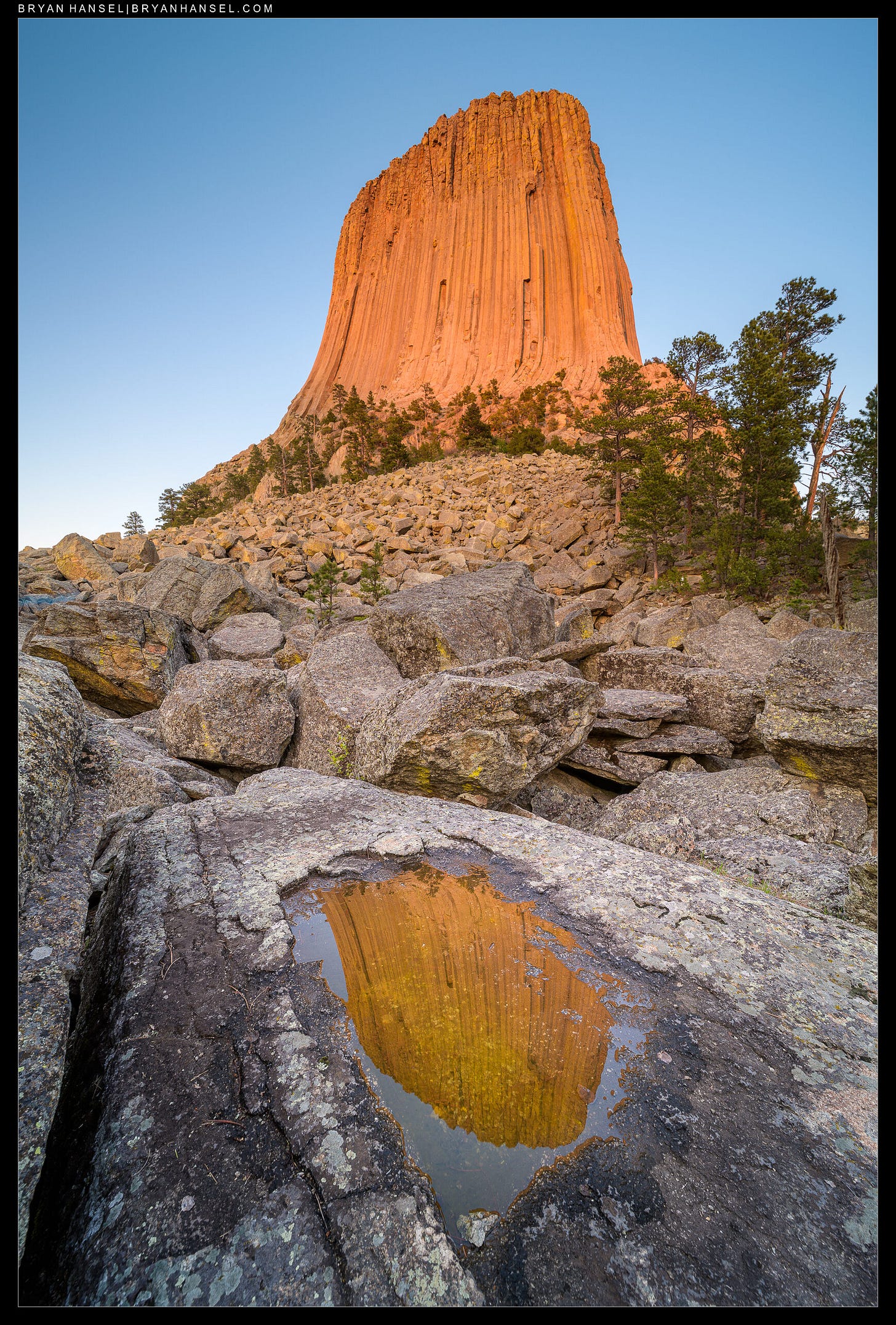 Devils Tower lit golden with the sunset and its reflection in a small puddle below. Devils Tower lit golden with the sunset and its reflection in a small puddle below.