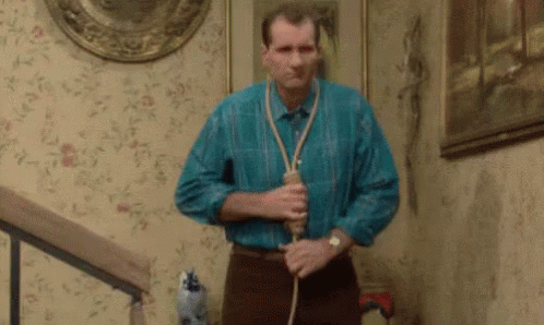a man in a blue shirt is holding a rope around his neck while standing on a set of stairs . a man in a blue shirt is holding a rope around his neck while standing on a set of stairs .