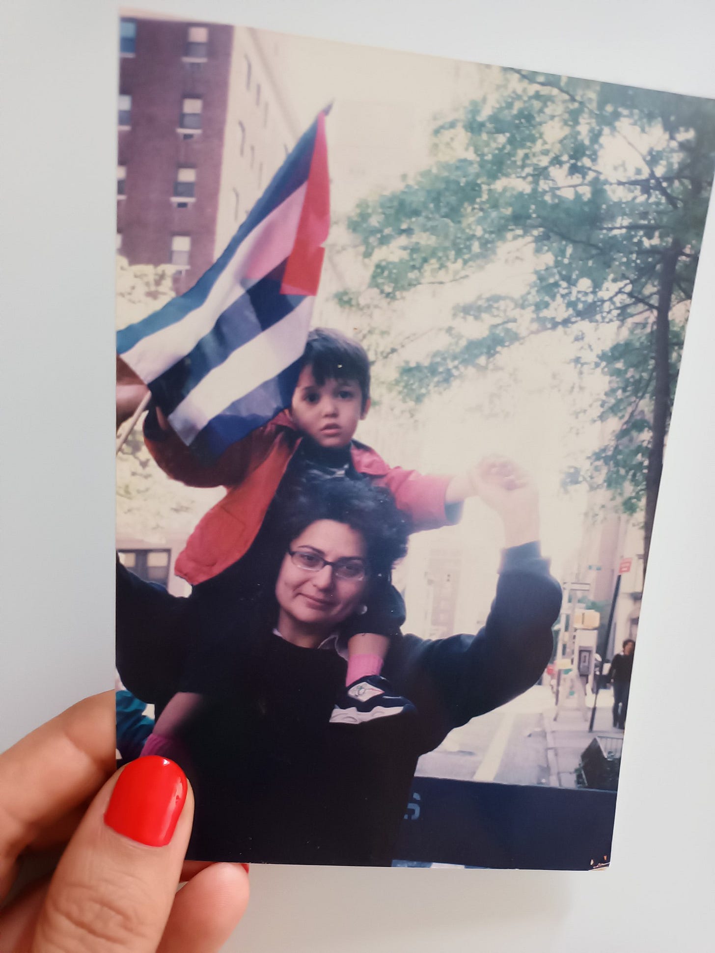 Una mano sostiene foto de papel de una mujer que lleva a hombros a un niño que ondea una bandera cubana.