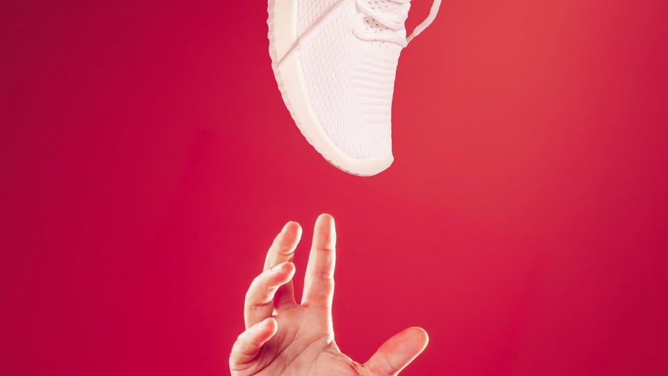 An image of a hand reaching for a sneaker against a red background. An image of a hand reaching for a sneaker against a red background.