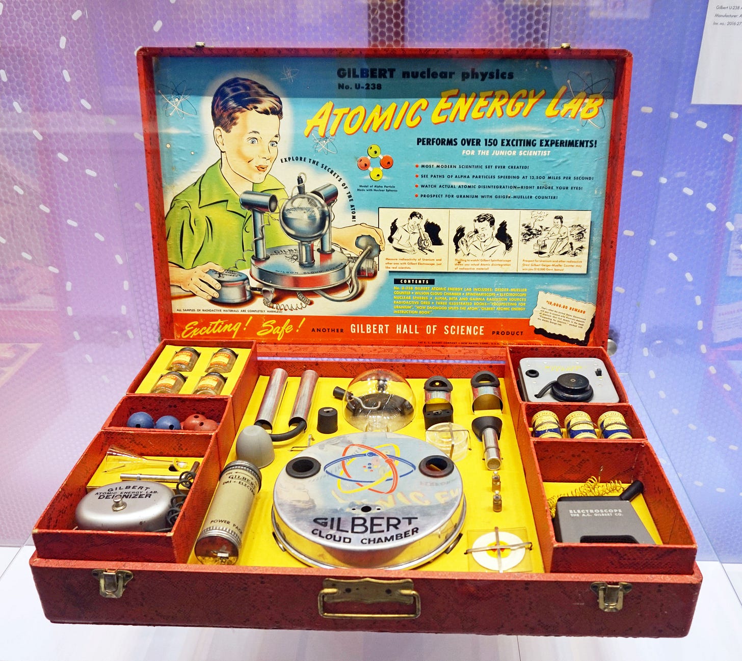 A red suitcase showing the contents of the toy Atomic Energy Lab. Inside many peices designed to conduct the experiments