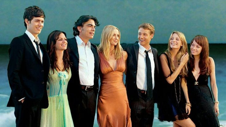 This may contain: a group of people standing next to each other near the ocean with one woman in a long dress
