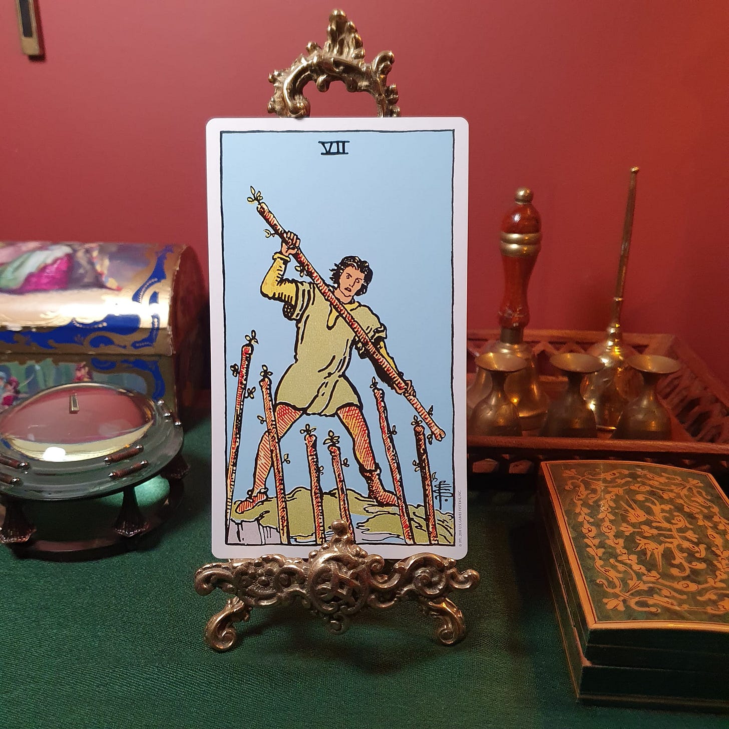Seven of Wands tarot card displayed on an ornate stand during Jill Dawson’s Tarot DMs Chat 42, with tarot and divination objects in the background.