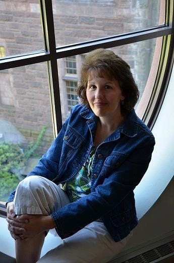Photo of Julie Moore sitting on a windowsill in a denim jacket and smiling