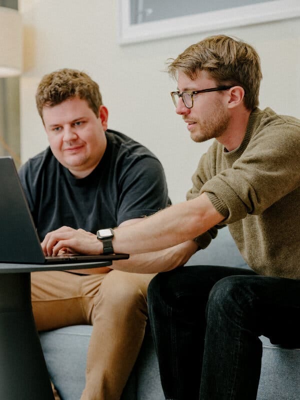 Nick Turley, left, wearing a dark T-shirt, and Johannes Heidecke, wearing a light brown sweater look at a laptop computer.