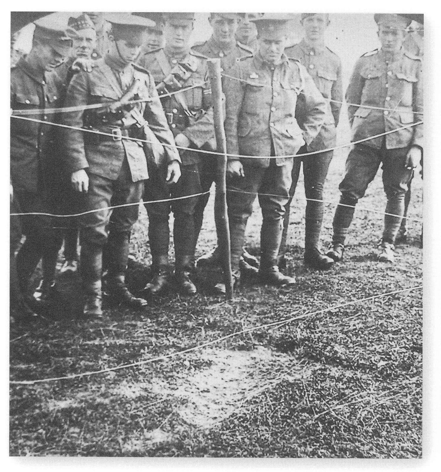 Armed Forces personnel stand behind a makeshift fence, looking at the impression left in the ground by a German crewmember who jumped from the burning zeppelin.