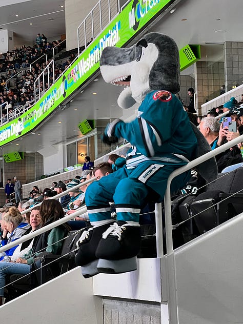 images of hockey arena, 2 girls wearing masks, a mascot shark on ice