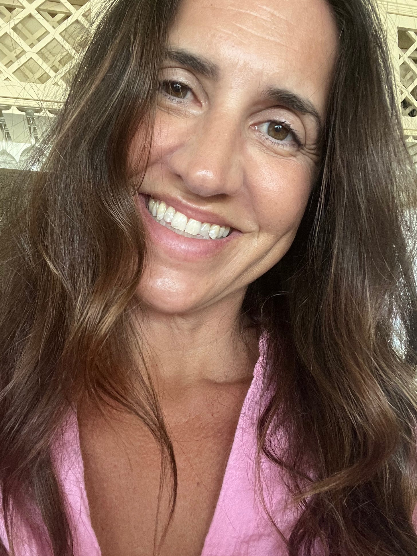 A close-up, natural and unretouched portrait of a smiling woman with long brown hair, showing a genuine, radiant expression and healthy skin texture."