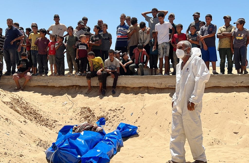 People watch as some of the 84 bodies of Palestinians handed over by Israeli forces are buried in a mass grave, in Khan Younis, southern Gaza Strip, on August 5, 2024. (Photo: Abdullah Abu Al-Khair / APA Images)