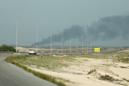 A highway with black smoke billowing in the distance 